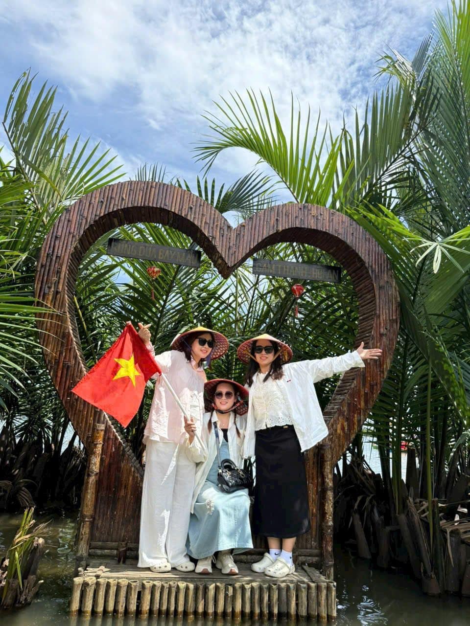 Three travellers in a heart-shaped bamboo frame with the Vietnamese flag and palms behind
