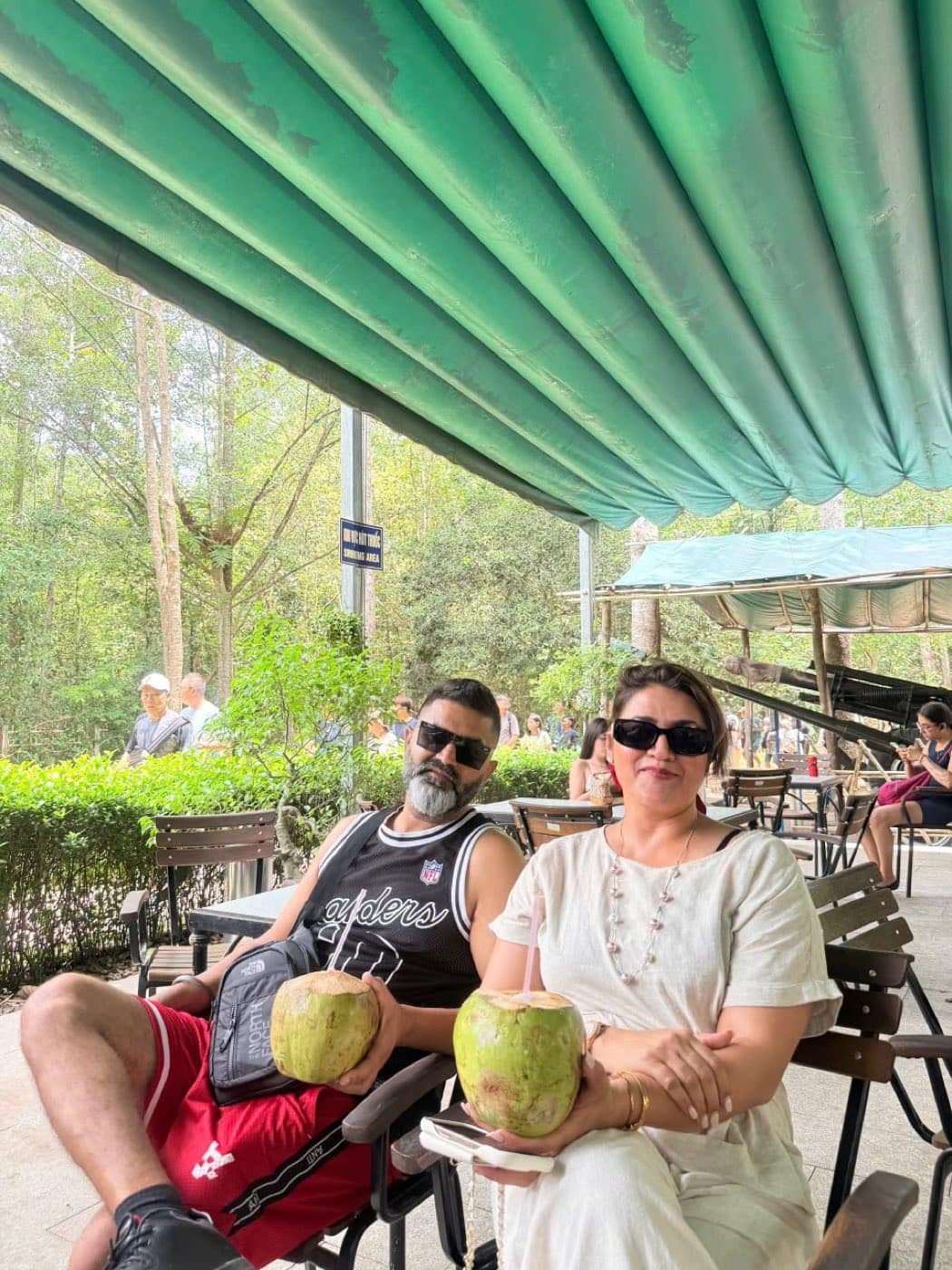 Two guests with fresh coconuts at the shaded rest area after the tunnels
