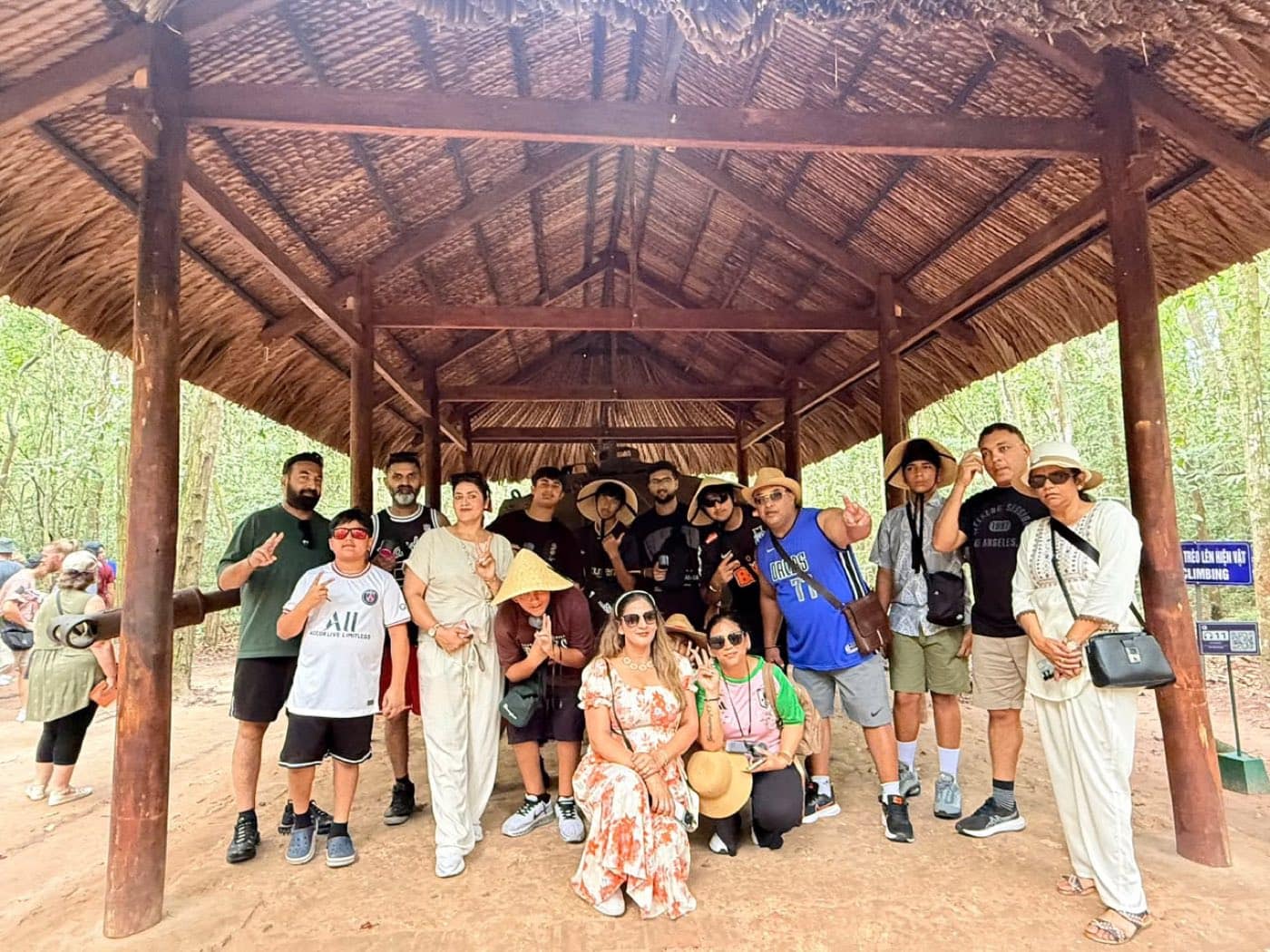 A full tour group under the thatched shelter in the rubber trees