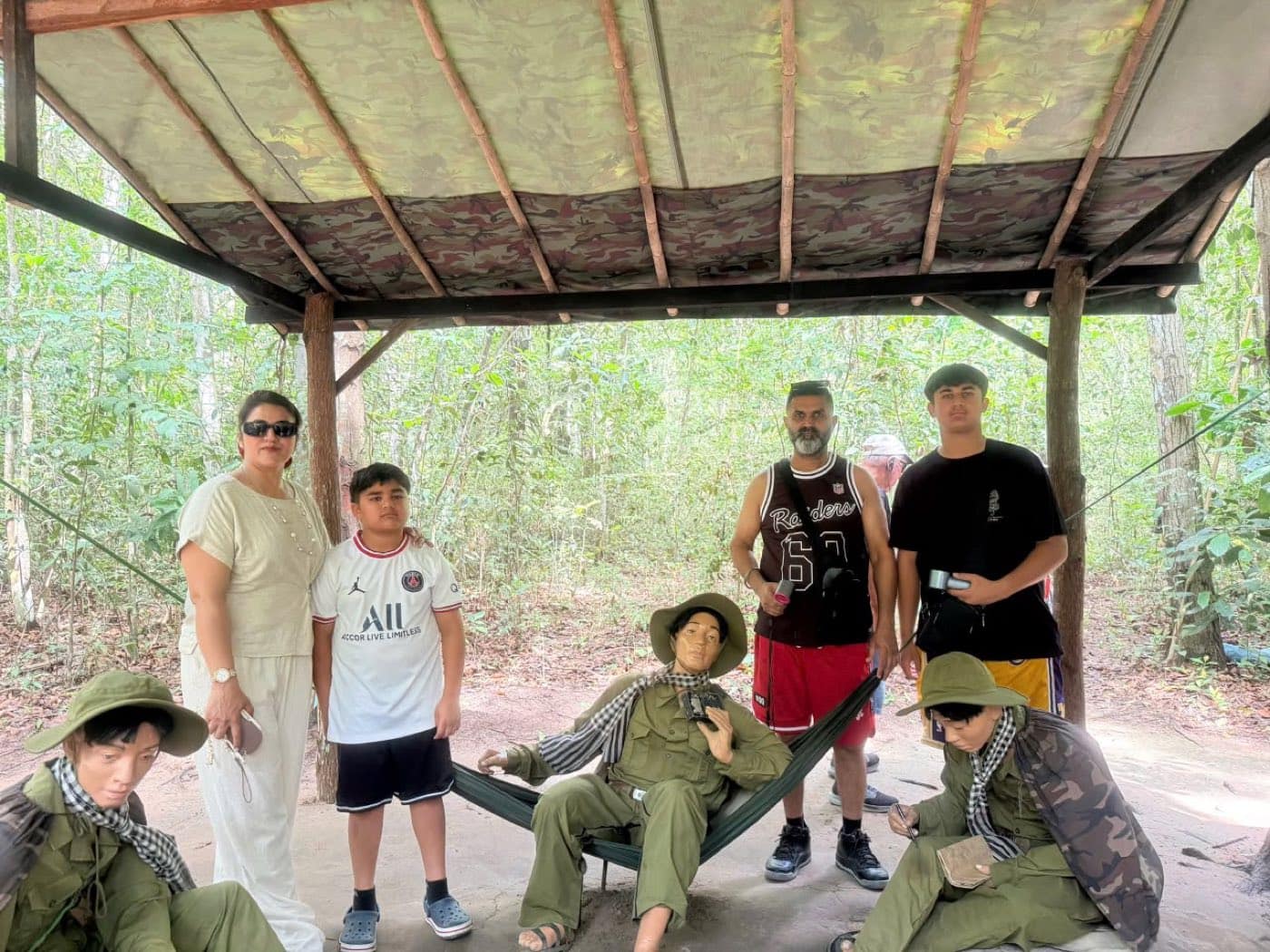 Guests beside the uniformed figures set out under a camouflage-netting shelter