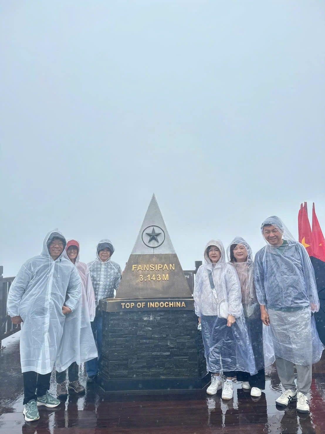 Guests in rain ponchos at the Top of Indochina marker on the summit