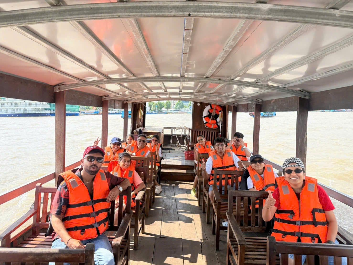 Guests in orange life vests on the bench seats of a Mekong river boat