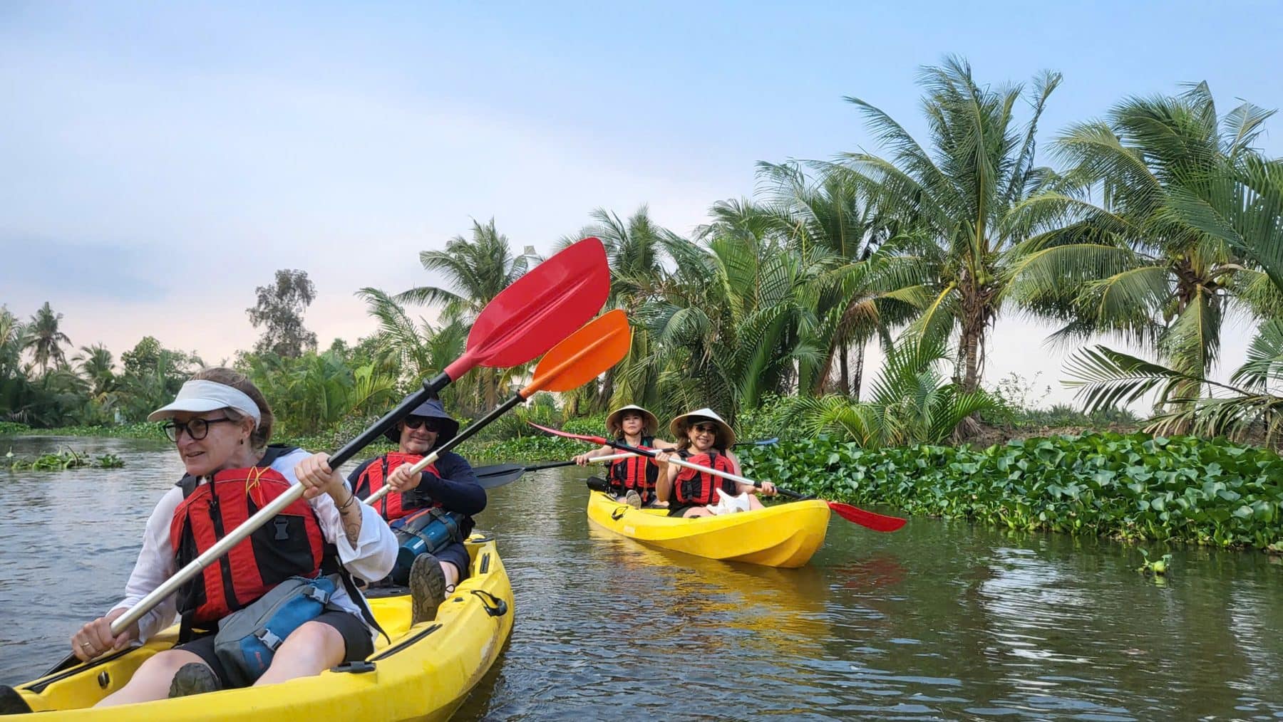 Kayakers following a narrow canal between the water palms