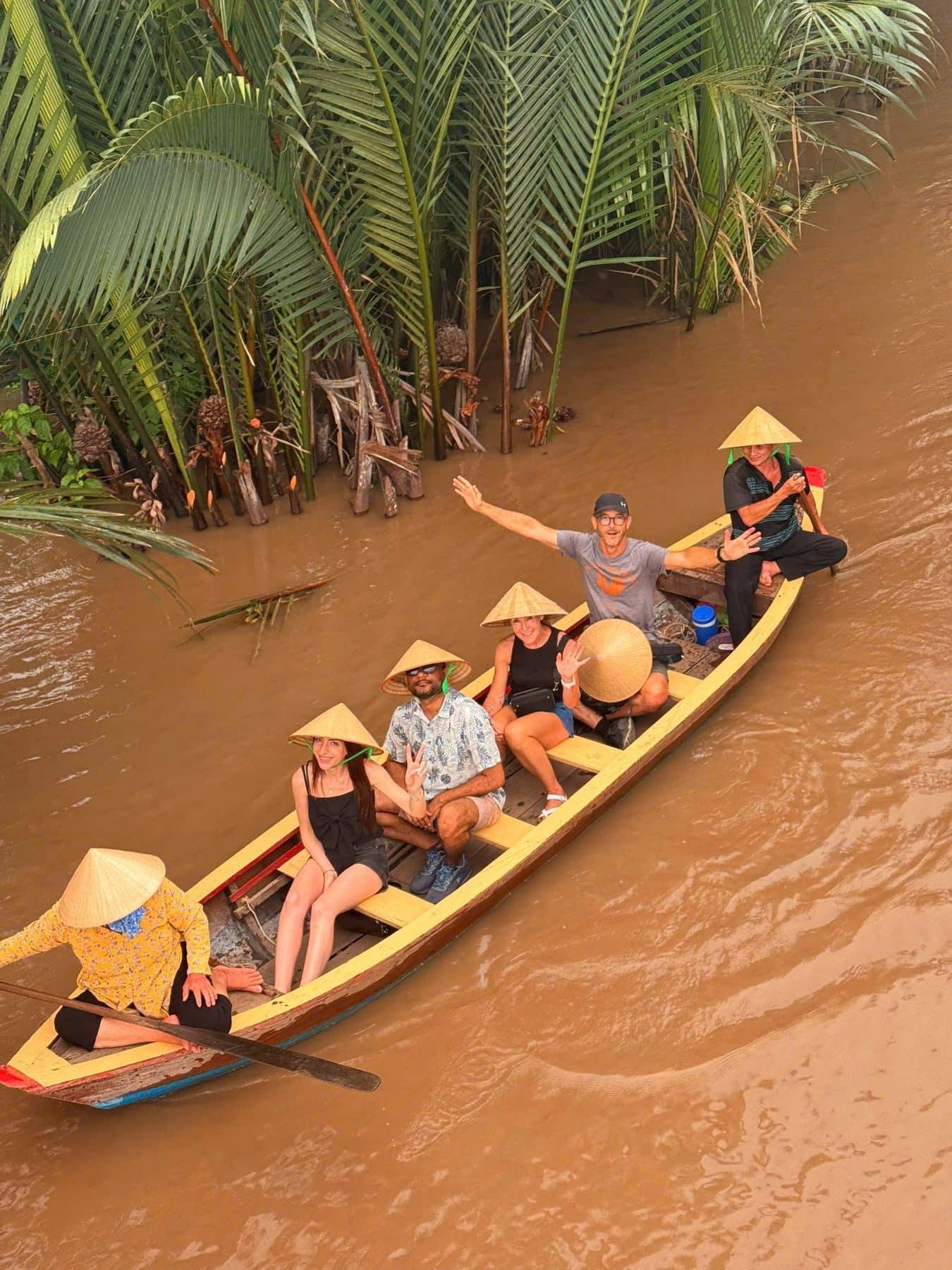 A wooden boat of guests in conical hats on the brown river water