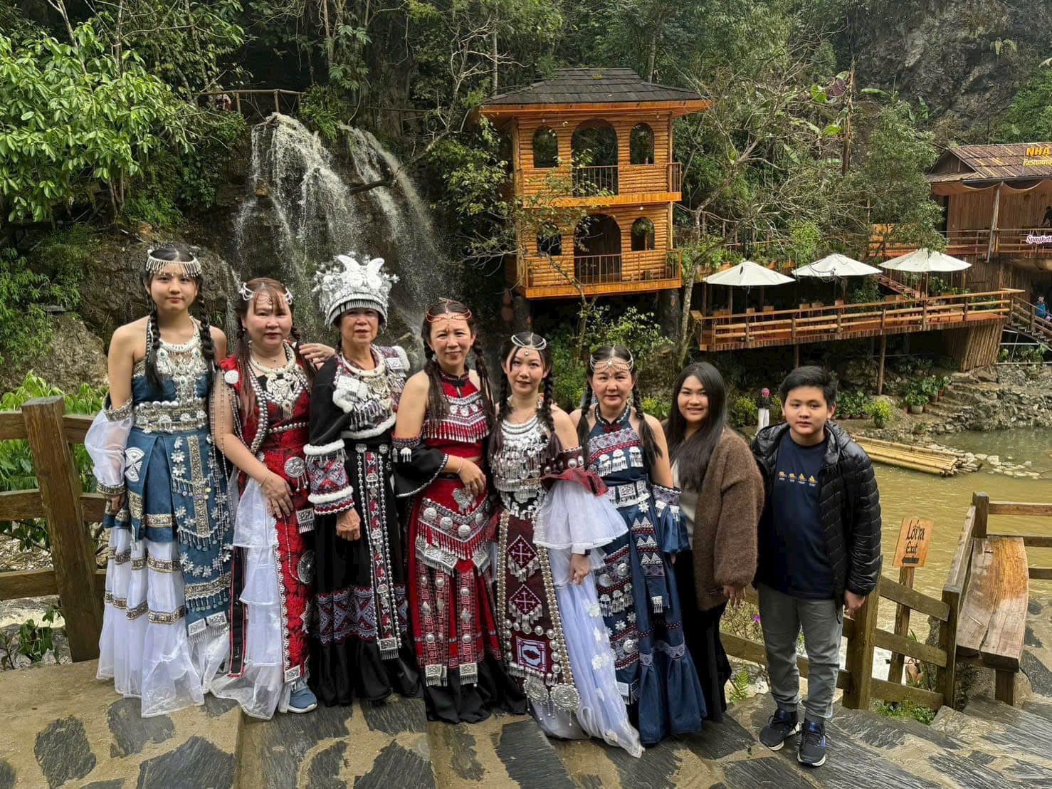 Travellers in highland dress beside the wooden village houses and waterfall