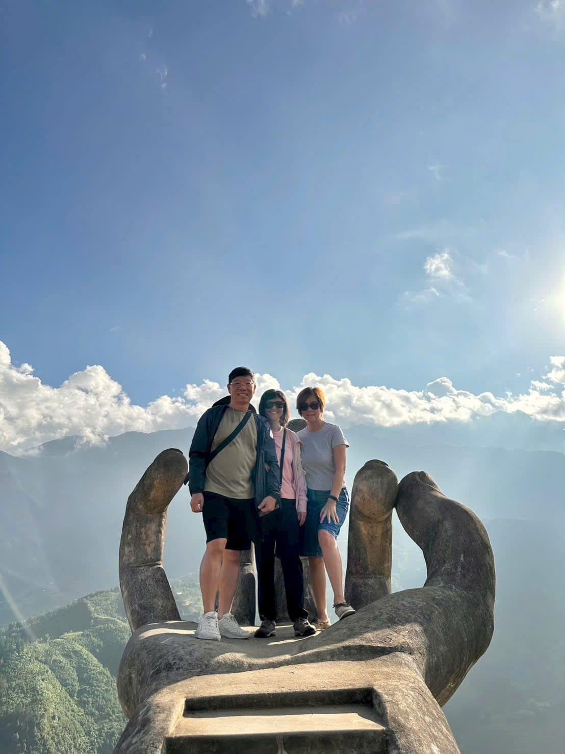 Three guests standing in the palm of the stone hand, the valley clouding over below