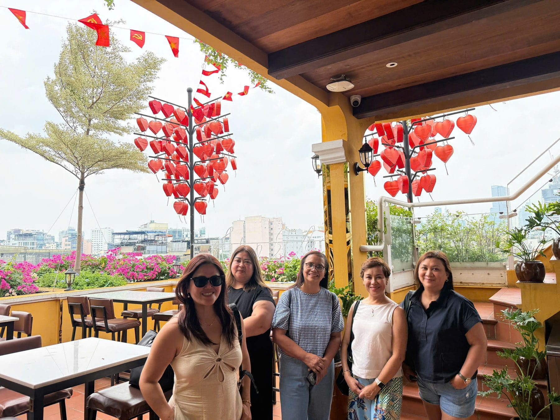Five travellers together on a cafe terrace hung with red paper hearts and lanterns