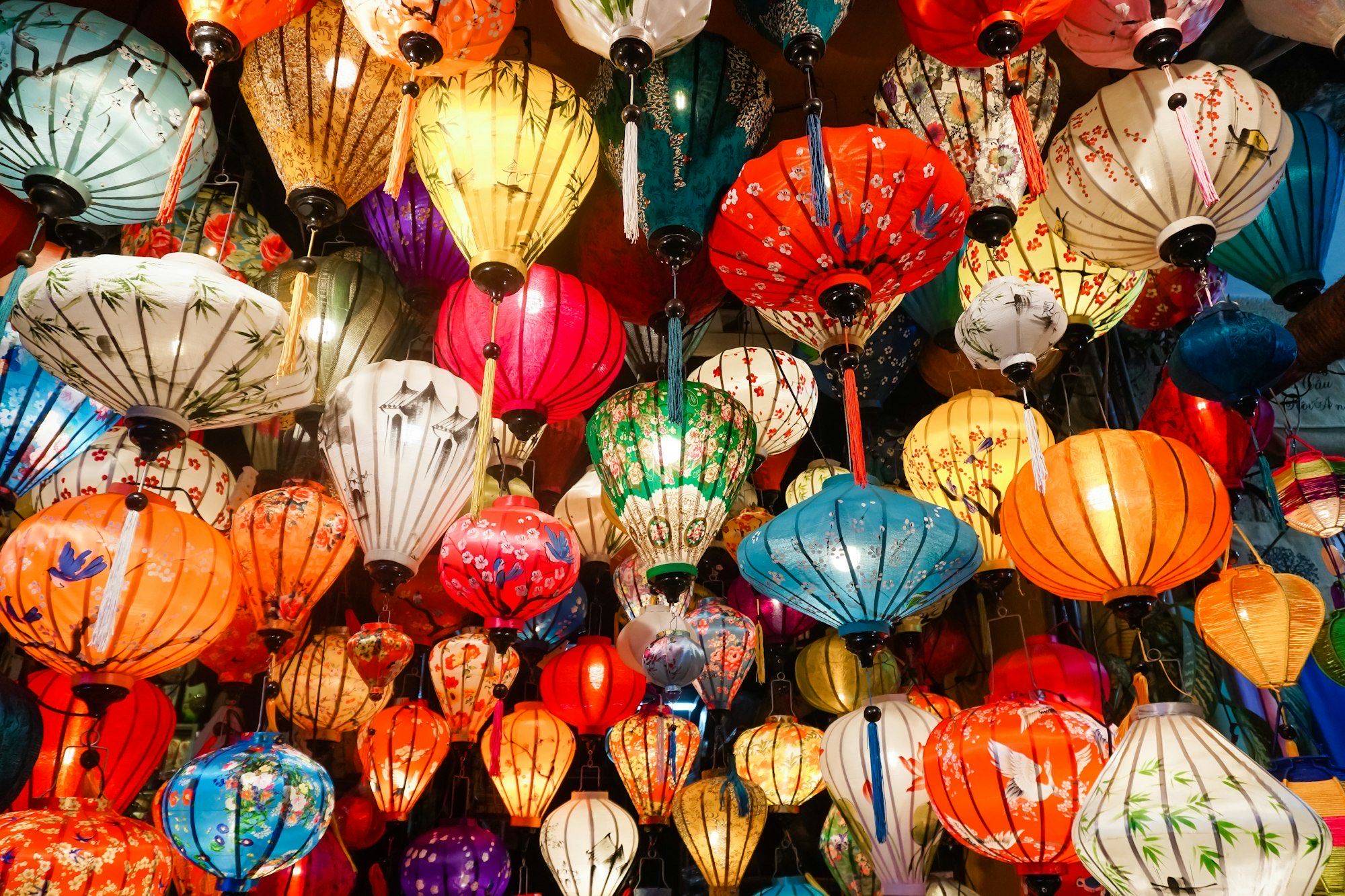Dense canopy of glowing hand-painted silk lanterns in red, orange, teal and white in a Hoi An shop
