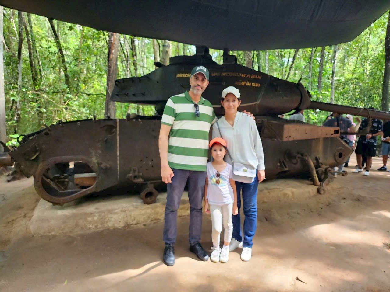 A family beside the wrecked tank under the trees at Cu Chi