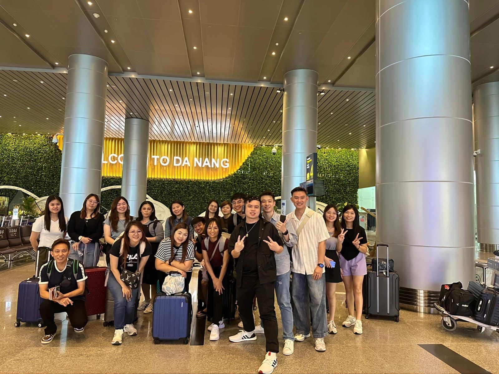 A tour group with their suitcases under the Welcome to Da Nang sign in the airport arrivals hall