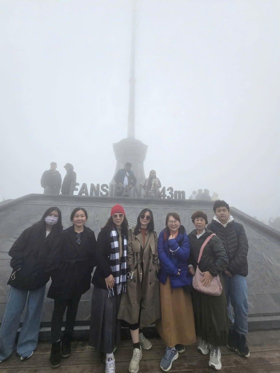 A group at the Fansipan 3,143m summit marker in thick fog