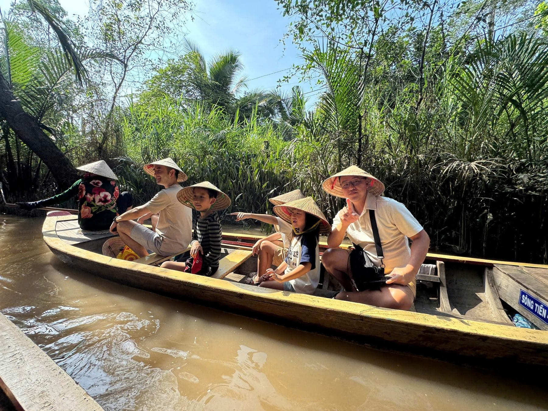 Guests in conical hats on a hand-rowed sampan under the water coconut trees